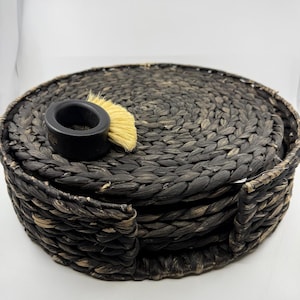 Könnte beinhalten: Ein Set aus vier schwarzen geflochtenen Untersetzern mit einer schwarzen Bürste mit Naturborsten und einem schwarzen Ringhalter.