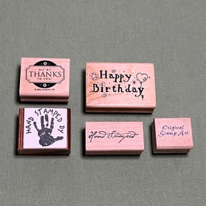 Pode incluir: Quatro carimbos de borracha de madeira com designs diferentes. O primeiro carimbo diz "All My Thanks To You!" O segundo carimbo diz "Happy Birthday". O terceiro carimbo diz "Hand Stamped". O quarto carimbo diz "Original Stamp Art".