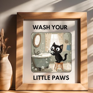 Peut inclure: Une affiche encadrée avec le texte "WASH YOUR LITTLE PAWS". L'image montre un chat noir dans une salle de bain, se lavant les pattes dans une baignoire. Le cadre est en bois brun clair, et un vase est visible à gauche.