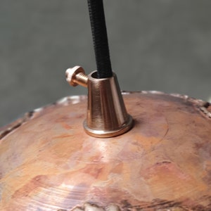 May include: Close-up of a copper pendant light fixture with a brass ceiling mount and black electrical cord.