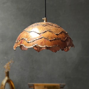 May include: A copper pendant light fixture with a wavy, textured shade. The shade is a warm copper color with hints of red and gold.