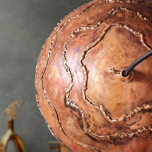 May include: A copper sphere pendant light fixture with a decorative, textured surface and a black wire cord. The fixture has a brass fitting for attaching a light bulb.