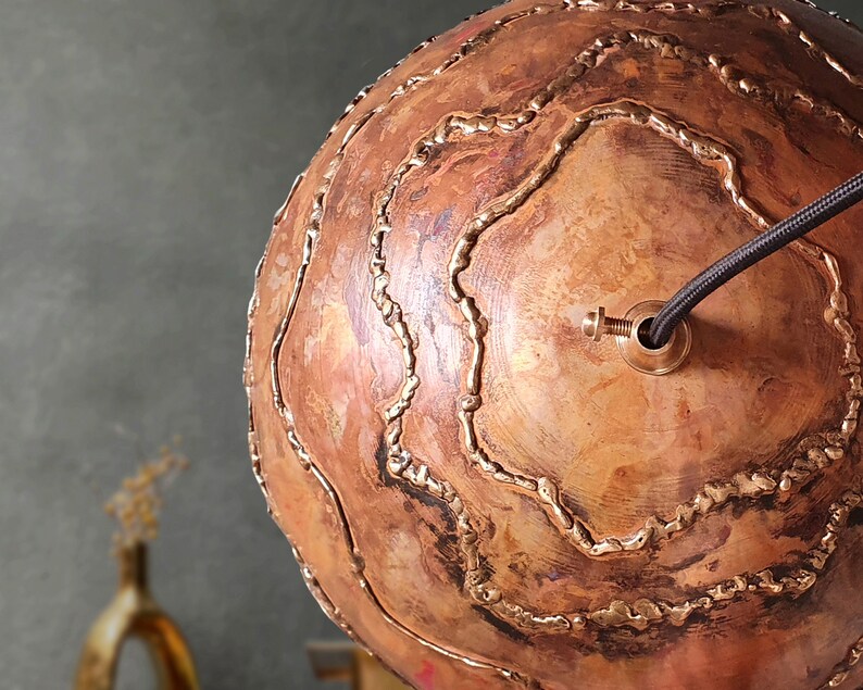 May include: A copper sphere pendant light fixture with a decorative, textured surface and a black wire cord. The fixture has a brass fitting for attaching a light bulb.