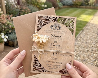 May include: A wooden wedding invitation with laser-cut floral designs, featuring the names Daniel and Emma, the date December 12, 2025, and the event location. The invitation is accompanied by a brown envelope and a small bouquet of dried flowers.