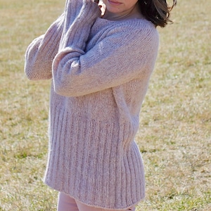 Może przedstawiać: Kobieta w jasnoróżowym, prążkowanym swetrze z długimi rękawami. Sweter jest luźny i ma swobodny, casualowy styl.