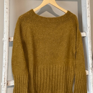 以下が含まれることがあります： マスタードイエローのニットセーター。ワイドネックで長袖。裾と袖口はリブ編みです。