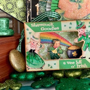 May include: A St. Patrick's Day themed display featuring a green glitter top hat, gold glitter ornaments, and a box with the text "Shamrock Goodies". The box has illustrations of leprechauns, a rainbow, and a pot of gold.