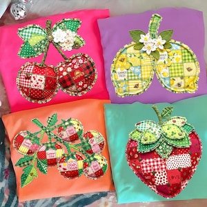 May include: Four colorful throw pillows with appliqued fruit designs. The pillows feature cherries, lemons, tomatoes, and a strawberry, each with a patchwork design. The cherry pillow is pink, the lemon pillow is purple, the tomato pillow is orange, and the strawberry pillow is teal.