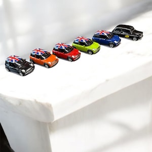 Könnte beinhalten: Eine Sammlung von Miniatur-Spielzeugautos in verschiedenen Farben, darunter Schwarz, Orange, Rot, Grün und Blau. Jedes Auto hat eine Union Jack-Flagge auf dem Dach. Ein schwarzes Taxi ist ebenfalls vorhanden.