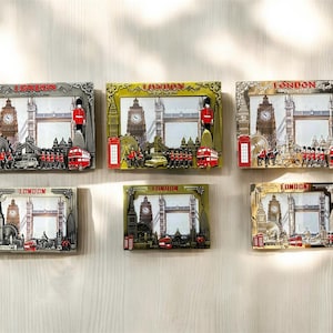 May include: Six silver and gold-toned picture frames with a London theme. Each frame features a red double-decker bus, a red telephone booth, and a depiction of Big Ben and Tower Bridge. The frames are all the same size and shape, but they have different colors and designs.