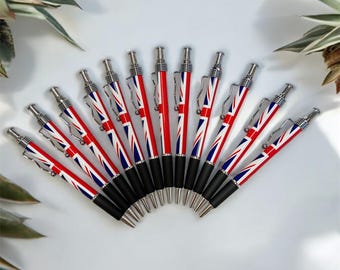 Puede incluir: Un conjunto de diez bolígrafos negros y plateados con un diseño de Union Jack. Los bolígrafos están dispuestos en semicírculo sobre una superficie blanca.