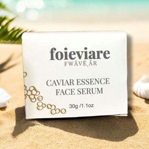 Może przedstawiać: Białe pudełko z nadrukowanym tekstem "foieviare FW&Auml;VE,&Auml;R" i "CAVIAR ESSENCE FACE SERUM 30g / 1.1oz". Pudełko leży na piaszczystej plaży.
