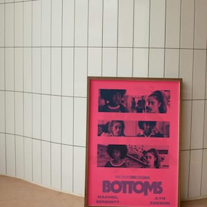May include: A framed movie poster with a pink background and the title "Bottoms" in bold purple text. The poster features four young women in different scenes, with the text "Directed by Emma Seligman" and the names "Rachel Sennott" and "Ayo Edebiri" below the title.