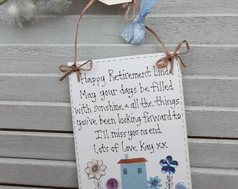 May include: A white card with a handwritten message that reads "Happy Retirement Linda May your days be filled with sunshine & all the things you've been looking forward to I'll miss you no end. Lots of love Kay xx". The card is decorated with a blue house, flowers, and buttons.