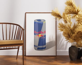 May include: A framed print featuring a stylized illustration of a Red Bull energy drink can. The can is primarily blue and silver, with the Red Bull logo in red and yellow. The print is displayed against a white wall, with a wooden chair and decorative dried plants in the background.