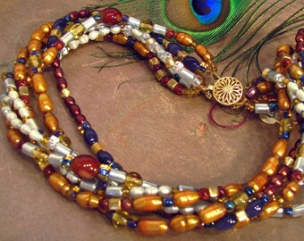 May include: Multi-strand necklace with brown, white, gold, silver, and blue beads. The necklace is made of various materials, including glass, metal, and plastic. The necklace is a beautiful and unique piece of jewelry.