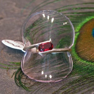 Puede incluir: Un anillo de plata con una sola piedra roja ovalada engastada en el centro.