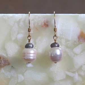 May include: A pair of gold dangle earrings with white pearls and a dark gray pearl accent.