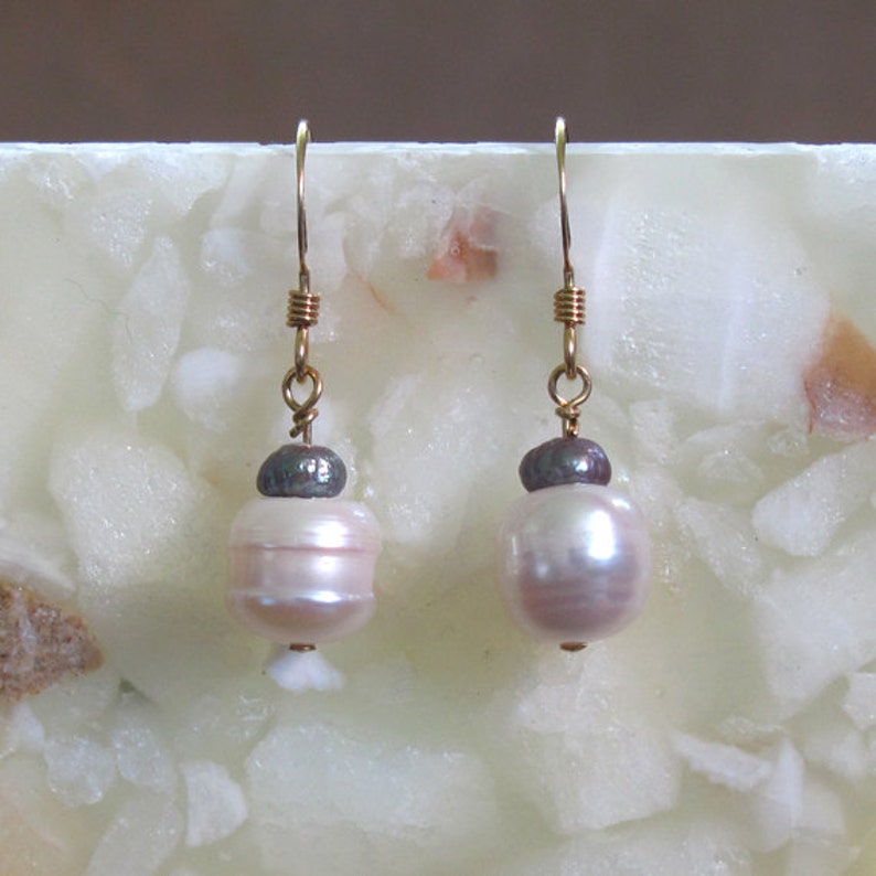 May include: A pair of gold dangle earrings with white pearls and a dark gray pearl accent.