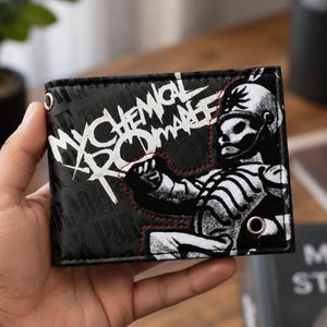 May include: A black bi-fold wallet featuring the white text My Chemical Romance and a graphic of a skeleton figure in a marching band uniform. The wallet includes two silver-toned metal grommets and is accented with red stitching along the design.