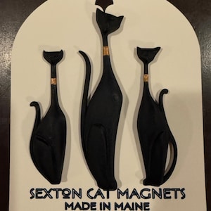 May include: Three black cat magnets with gold accents are displayed on a white card. The magnets are stylized with long necks and curved tails. The card reads "Sexton Cat Magnets Made in Maine."