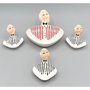 May include: A set of four ceramic dishes shaped like waiters with heads and torsos. One large dish features a red and white striped vest, while three smaller dishes feature black and white striped vests. Each waiter has a black bowtie and white shirt.