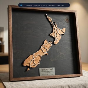 May include: A framed wall art piece featuring a layered wooden map of New Zealand against a dark charcoal background. The map includes white line details, a compass rose, and a plaque labeled NEW ZEALAND Land of the Long White Cloud.