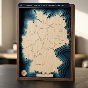 Pode incluir: Um mapa de madeira em camadas da Alemanha com um acabamento de madeira clara para as fronteiras do país e tons de azul profundo para a água circundante. A obra emoldurada inclui uma rosa dos ventos e uma etiqueta com o texto DEUTSCHLAND.
