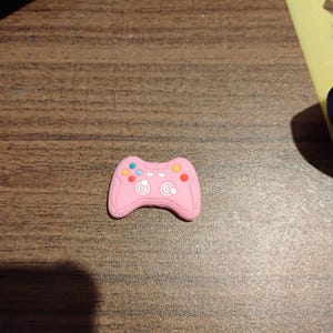 May include: A pink plastic video game controller charm with colorful buttons.