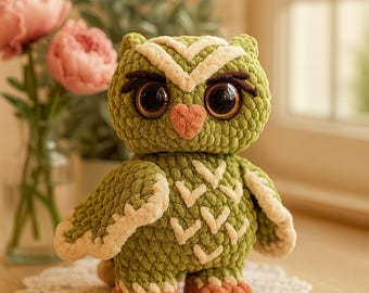 May include: A handmade green crochet owl with large, expressive eyes and a heart-shaped nose. The owl has cream-colored accents on its head, wings, and chest. Its feet are a soft orange color. The owl is standing on a white lace doily.