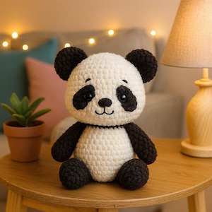 May include: A handmade crochet panda bear with a white body, black arms, legs, and ears, and black markings around the eyes. The panda is sitting on a wooden table. The panda is a cute, soft toy.