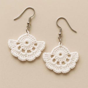May include: A pair of white, handmade crochet earrings. Each earring features a fan-shaped design with a central circle and decorative openwork. The earrings hang from silver-colored fish hook ear wires, showcasing a delicate, handcrafted aesthetic.