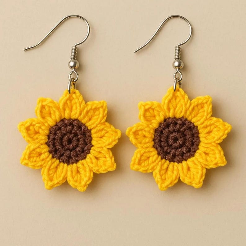 May include: A pair of handmade crochet sunflower earrings. Each earring features a bright yellow crocheted flower with a dark brown center. The earrings have silver-colored fish hook ear wires.