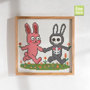 May include: Cross-stitch artwork in a wooden frame depicting two cartoon rabbits. One is pink, the other is grey with a skeleton design. They hold hands and run through a field of flowers. The artwork has a whimsical, playful theme.