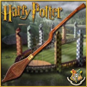 May include: A brown wooden broomstick with gold accents and a brown bristle brush. The broomstick is in front of a blurred background of a Quidditch field with goal posts and a golden snitch.