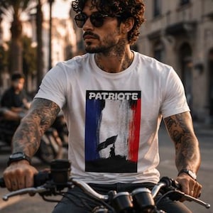 Peut inclure: T-shirt blanc avec le mot "PATRIOTE" au-dessus d'un drapeau français stylisé et d'une silhouette. La personne porte le t-shirt et conduit une moto.