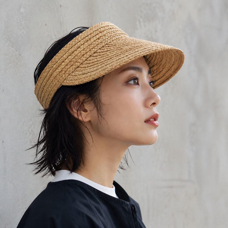 Side view of a woman wearing a wide brim raffia straw sun visor with open top for ponytails