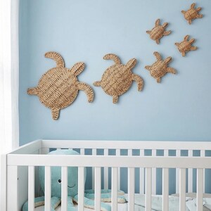 A nursery room with a white crib and a blue stuffed animal. Above the crib, there are three woven turtle-shaped wall decorations.