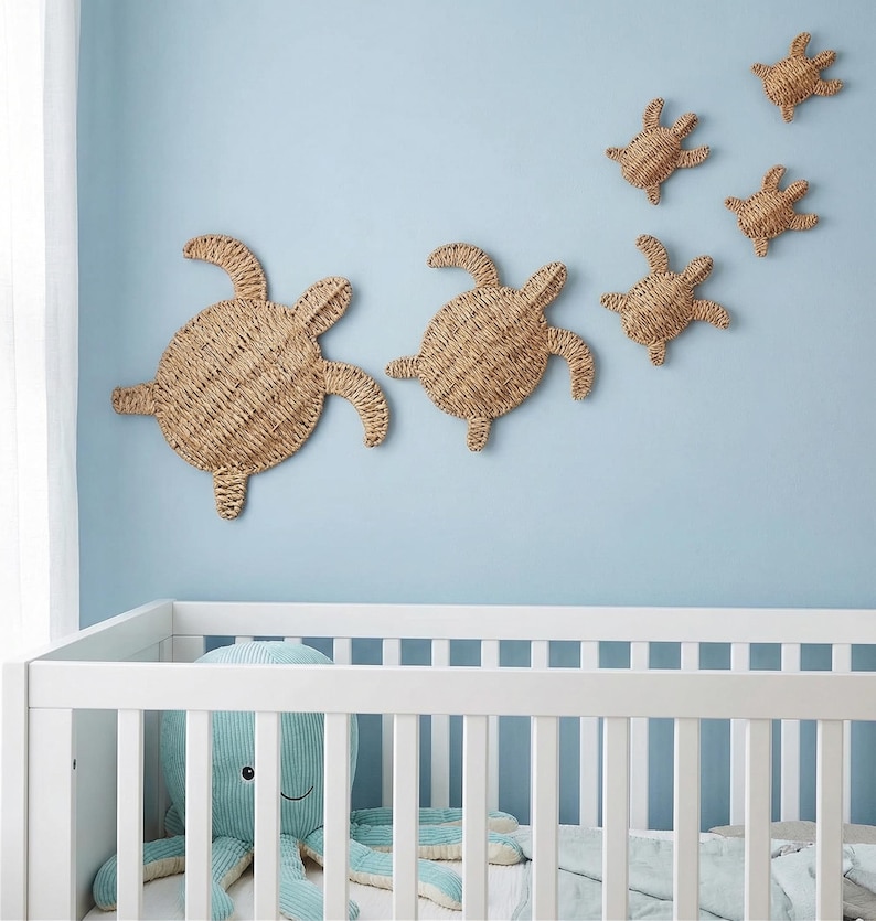A nursery room with a white crib and a blue stuffed animal. Above the crib, there are three woven turtle-shaped wall decorations.