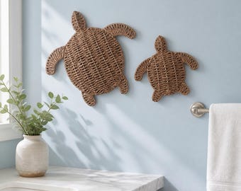 May include: Two wall-mounted sea turtle decorations crafted from woven brown natural fibers. The larger turtle is positioned to the left of the smaller turtle, both featuring detailed shell patterns and extended flippers in a flat design.