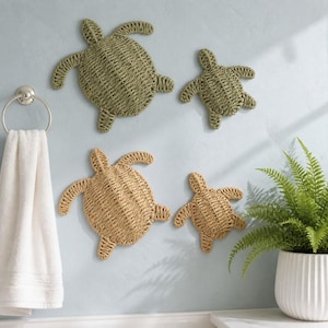 May include: Four sea turtle wall decorations crafted from woven natural fibres. Two turtles are coloured in a muted sage green, while the other two are in a light tan shade. Each turtle features a textured, braided pattern across its shell and limbs.