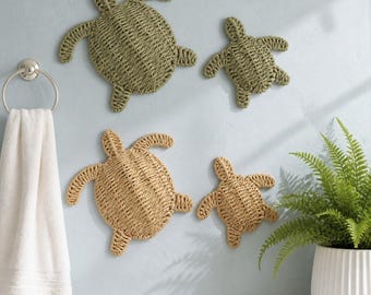 Puede incluir: Cuatro decoraciones de pared con forma de tortuga marina hechas de fibras naturales tejidas. Dos tortugas son de color verde salvia suave, mientras que las otras dos son de un tono beige claro. Cada tortuga presenta un patrón trenzado en su caparazón.