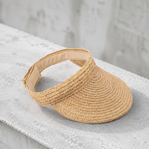 Packable handwoven raffia straw visor hat with adjustable closure on a concrete ledge