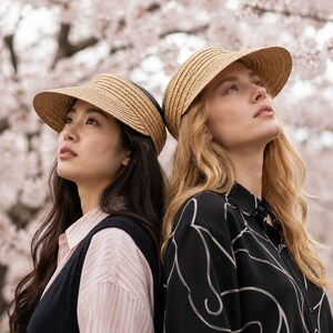 Two women wearing adjustable raffia straw sun visors under cherry blossoms