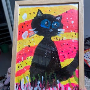 Puede incluir: Una pintura enmarcada de un gato negro con ojos azules brillantes sentado en un campo de flores amarillas, rosas y blancas. El fondo es un diseño abstracto colorido.