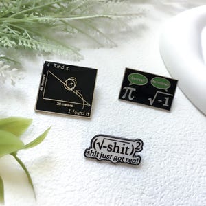May include: Three black enamel pins with white and green text. One pin reads "4 Find x" with a diagram and "I found it." Another pin features "π" and "√-1" with speech bubbles. The third pin says "(√-shit)² shit just got real."