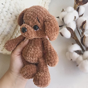 Puede incluir: Un peluche de perro cachorro de ganchillo marrón hecho a mano con ojos negros y una nariz negra. El peluche es suave y tierno, con orejas caídas y una expresión linda. El perro mide aproximadamente 20 cm de alto.