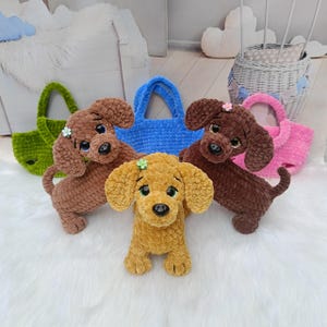 May include: A collection of handmade crochet dog toys in various colors, including brown, yellow, and green. Each dog has large, expressive eyes and a small flower accessory. Several matching tote bags in blue and pink are also visible.