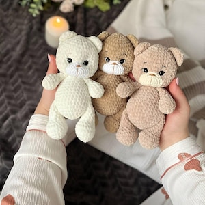 Peut inclure: Trois ours en peluche crochetés à la main, de couleur crème, beige et marron clair. Chaque ours a un visage cousu avec des yeux noirs et un museau blanc. Les ours sont doux et moelleux, parfaits pour une chambre d'enfant ou comme cadeau.