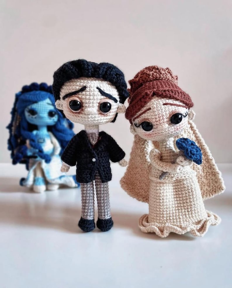 Puede incluir: Mu&ntilde;ecos de ganchillo de personajes de una pel&iacute;cula de animaci&oacute;n stop-motion. Los mu&ntilde;ecos incluyen un novio con chaqueta negra y pantal&oacute;n gris, una novia con vestido y velo color crema, y un personaje azul con pelo azul y vestido blanco.